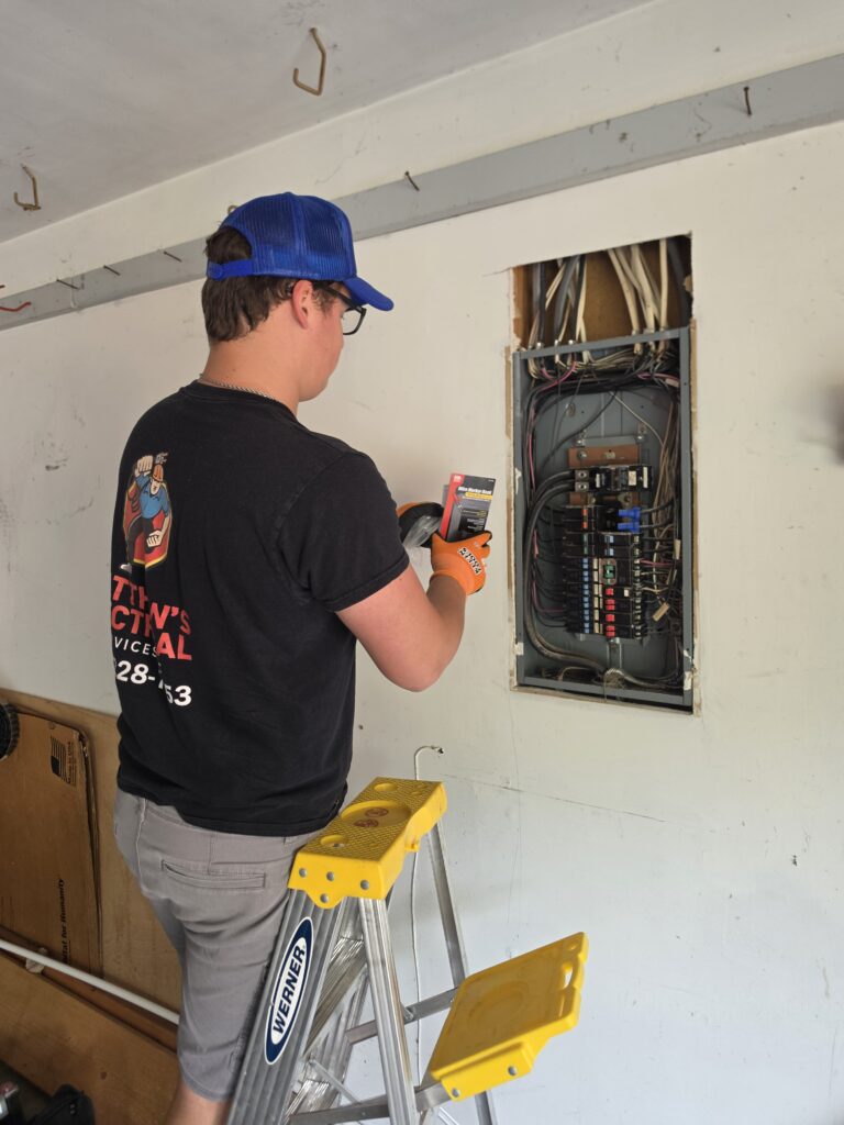Electrician on a step ladder testing an open panel with a meter