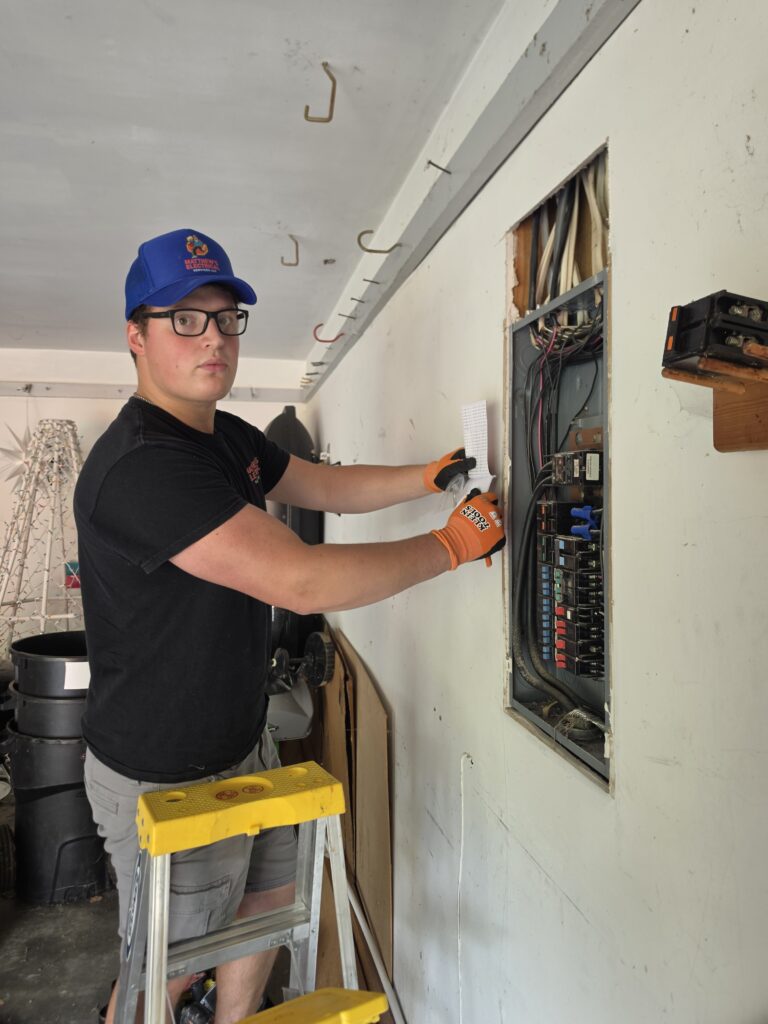Electrician on a ladder beside an open electrical panel in Charlotte