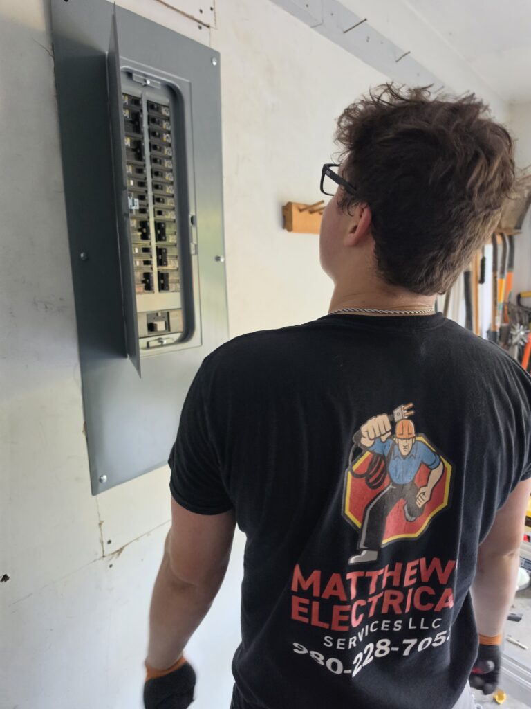 Matthews Electrical electrician standing by an open electrical panel