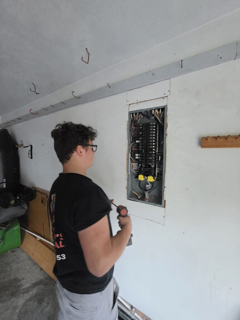Electrician with a screwdriver servicing a recessed garage panel