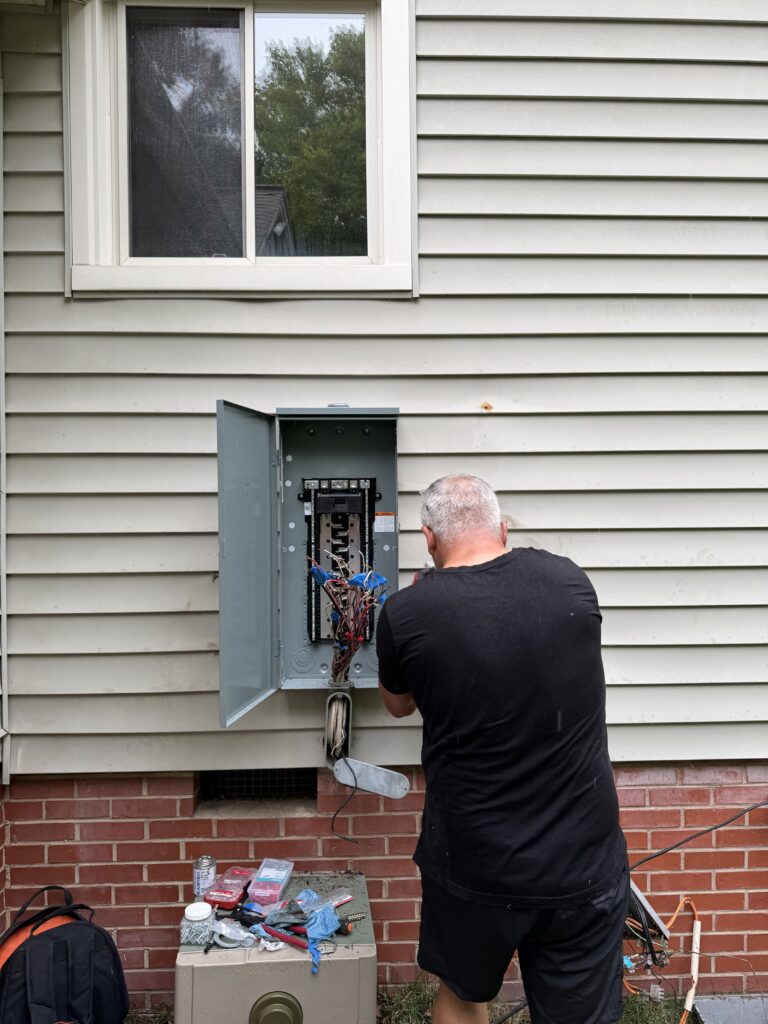 Electrician wiring an open outdoor electrical panel on a Charlotte home