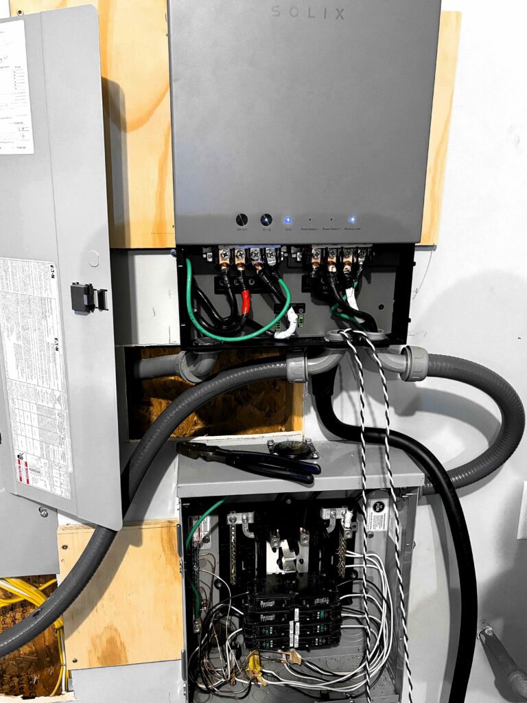 Wall-mounted backup power unit wiring above a sub-panel in conduit