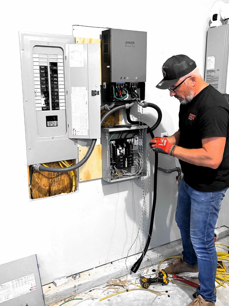 Electrician connecting a cable to a backup power unit beside a panel