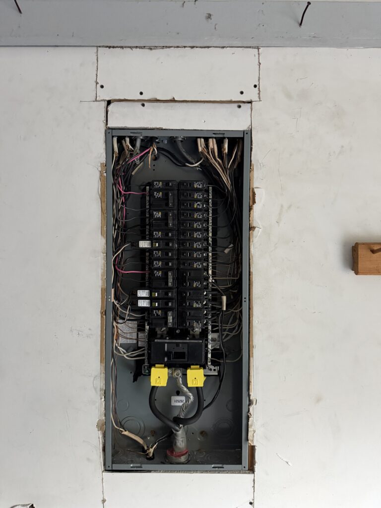 Open electrical panel with breakers set into a patched garage wall